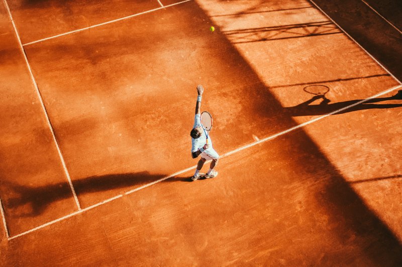 Tennisser slaat een service op een gravelbaan, van bovenaf